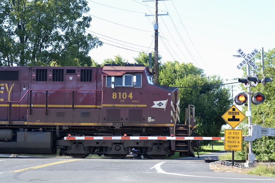 A locomotive passes a railroad crossing with the gate down and warning lights activated.