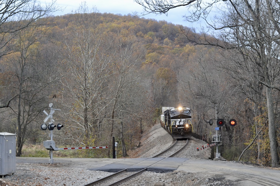 A train approaches a railroad crossing during the late fall season.