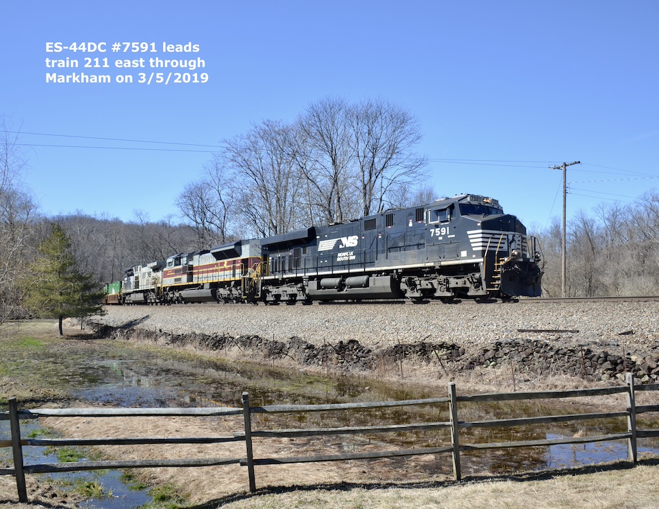 A Norfolk Southern freight train passes a rustic fence